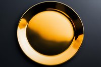 Elegant golden metallic plate with reflective surface on dark background for luxury dining and premium tableware presentations.