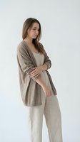 Young woman with long brown hair and fair complexion wearing casual linen clothing, including a beige cardigan and cream pants, standing against white background for fashion and lifestyle use.