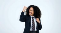 Young African American businesswoman celebrating success with raised fists and joyful expression in professional suit and tie on white background.