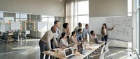 Diverse group of professionals collaborating around table in modern office with whiteboard, laptops, and natural light during business meeting or brainstorming session.