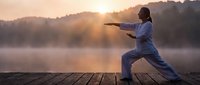Asian woman practicing tai chi on wooden dock at sunrise over misty lake with mountains in background for wellness and meditation concepts.
