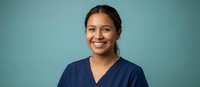 Happy young Hispanic female healthcare worker in navy scrubs smiling confidently against teal background for medical professional portraits and wellness campaigns.