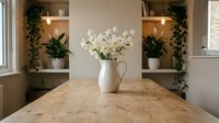 White ceramic pitcher with delicate flowers on wooden table in modern kitchen with green plants and warm lighting for home decor and interior design.