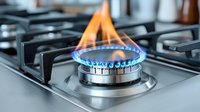 Gas stove burner with bright blue and orange flames on modern kitchen cooktop, close-up view showing heat intensity and energy consumption concept.