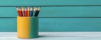 Colorful wooden pencils in yellow holder against turquoise blue wooden wall background, minimalist office supplies composition on white wooden table.