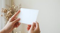 Woman's hands holding blank white card with dried flowers and bokeh lights in background for greeting or invitation mockup.