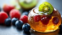 Fresh fruit jelly dessert with kiwi slice, raspberries and blueberries on dark background. Vibrant colors and selective focus create appetizing mood.