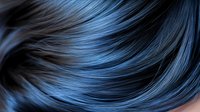 Flowing strands of dark blue and black hair create smooth waves and curves against dark background, showing silky texture and professional hair coloring technique.