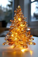 Illuminated crystal Christmas tree ornament with warm golden lights glowing through amber-colored glass, creating magical holiday atmosphere on white surface.