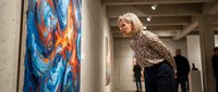 Blonde woman in leopard print top admiring colorful abstract artwork in modern gallery space with concrete walls and professional lighting.