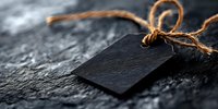Empty black price tag with twine string on dark stone background, dramatic moody lighting creates mysterious atmosphere for retail and marketing designs.