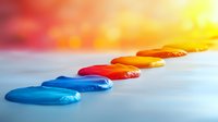 Colorful paint drops arranged in gradient line from blue to yellow on white surface with soft bokeh background creating artistic composition.