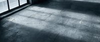 Empty concrete floor with natural light streaming through windows creating dramatic shadows in industrial interior space for construction projects.