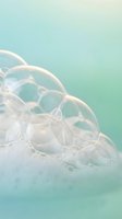Transparent soap bubbles floating on soft mint green background creating dreamy ethereal atmosphere for spa wellness and relaxation concepts.