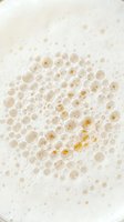 Closeup of foam bubbles with golden honey particles suspended in creamy liquid, ideal for beverage, skincare, and cosmetic product advertising.