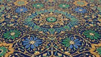 Ornate Islamic geometric pattern with intricate floral motifs in blue, green and gold colors on traditional decorative tilework surface.