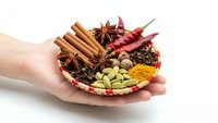 Hands holding wicker basket with aromatic spices including cinnamon sticks, star anise, cardamom, turmeric and chili peppers for cooking.