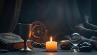 Mystical fortune telling setup with tarot cards, crystal ball, burning candle and ancient symbols creating atmospheric divination scene for spiritual practices.
