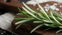 Fresh rosemary sprigs with water droplets on rustic wooden cutting board, ideal for culinary, cooking, and food styling projects.