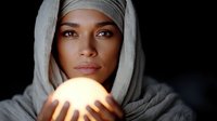 Young mixed-race woman in gray hoodie holding glowing orb of light in cupped hands against dark background for mystical spiritual energy concepts.
