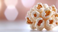 Delicate white crochet flower with intricate pattern on soft pink background, showcasing handmade textile art for home decor or fashion accessories.