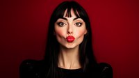 Young woman with long dark hair and red lipstick making kiss face expression against burgundy background, fashion portrait with dramatic lighting and minimal style.