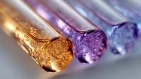 Glass test tubes with colorful liquid and bubbles in golden, purple and blue colors arranged in row, macro photography showing scientific research details.