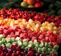 Fresh colorful fruit platter with strawberries, watermelon, cantaloupe, honeydew melon, and grapes arranged in decorative rows for catering and events.