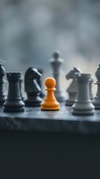 Single orange pawn stands out among black chess pieces on board with blurred background representing leadership, strategy, and standing out from crowd.