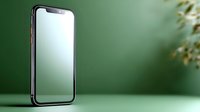 Modern smartphone with blank screen on green background with soft natural shadows and blurred plant elements creating minimalist composition.