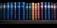 Row of vintage leather-bound books in various shades of blue, brown and purple arranged on dark wooden shelf, creating atmospheric library panorama.