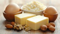 Fresh dairy butter blocks with cottage cheese, brown eggs in wooden bowls, walnuts and almonds on rustic wooden table. Natural healthy fats and protein sources for cooking.