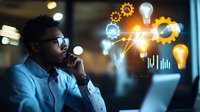 Young African American businessman in glasses working late at computer with glowing innovation icons, gears, and lightbulbs floating above in modern office setting.