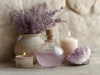 Aromatic lavender bouquet with burning candles, glass bottle of essential oil and amethyst crystal on wooden surface against textured wall, spa wellness concept.