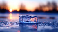 Translucent ice crystal formation on frozen lake surface at sunset with golden bokeh lights reflecting on melting surface creates magical winter atmosphere.