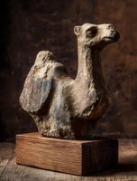 Ancient stone camel figurine on wooden base against dark brown background, showcasing archaeological artifact with weathered texture.
