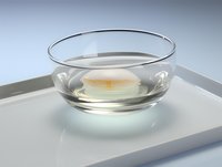 Floating white candle in clear glass bowl with water on minimalist gray tray, creating serene spa atmosphere. Clean composition for wellness and meditation concepts.