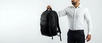 Man in white shirt holding black backpack against white background, suitable for business, travel, and product promotion designs.