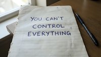 Handwritten motivational quote on lined paper saying you can't control everything with pen on wooden desk for mindfulness and acceptance concepts.