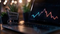 Shopping cart on laptop keyboard with financial chart on screen showing market volatility, blurred bokeh lights background creates business atmosphere.