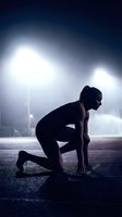 Athletic woman in starting position on track under dramatic stadium lights ready to sprint in competitive running race.