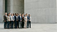 Diverse group of business professionals standing together in modern corporate setting with concrete architecture backdrop for team building and corporate communications.