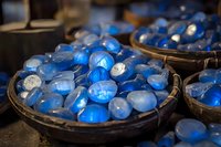Luminous blue gemstones and glass beads displayed in rustic wooden bowls create mystical atmosphere. Perfect for jewelry design, spiritual practices and decoration.