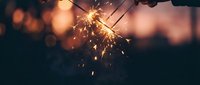 Sparkling sparkler burning brightly against blurred warm bokeh background at dusk, creating festive celebration atmosphere for holiday and event design projects.