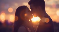Young couple sharing intimate moment at sunset with warm bokeh lights creating romantic atmosphere for wedding anniversary celebration.