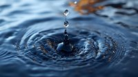 Single water drop creating concentric ripples on dark blue water surface with suspended droplets frozen in motion against blurred background. For nature and environmental themes.