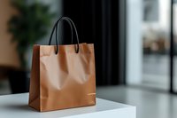 Brown kraft paper shopping bag with black handles on white surface, suitable for retail, e-commerce, packaging design, and shopping concepts.
