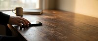 Professional businessperson using smartphone at wooden desk with coffee cup in warm office setting for communication and productivity.