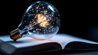 Glowing vintage light bulb with illuminated filament and decorative wire pattern resting on open book against dark background, symbolizing knowledge and inspiration.