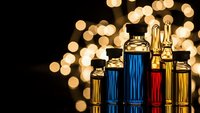 Luxury perfume bottles in gold, blue and red colors with warm bokeh lights creating elegant cosmetic product display for premium fragrance marketing.